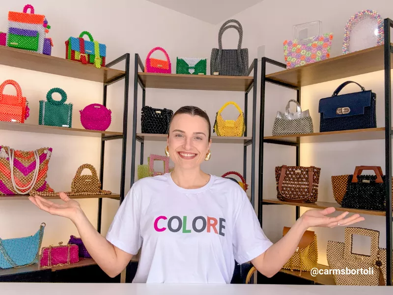 Mulher sorridente em frente a prateleiras de bolsas coloridas.