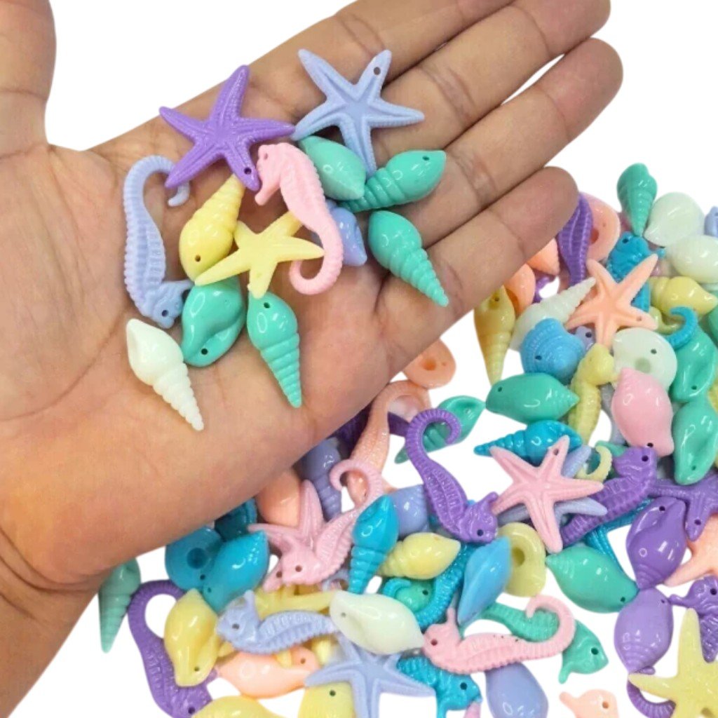 Várias miçangas em formato de vida marinha, como conchas, estrelas-do-mar e cavalos-marinhos, nas cores pastel.