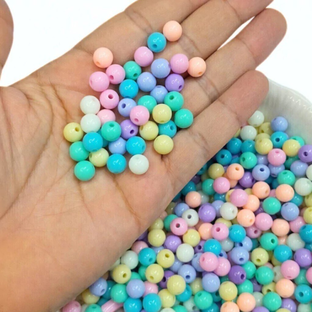 Muitas miçangas redondas e coloridas de plástico em tons pastel, sendo seguradas por uma mão.
