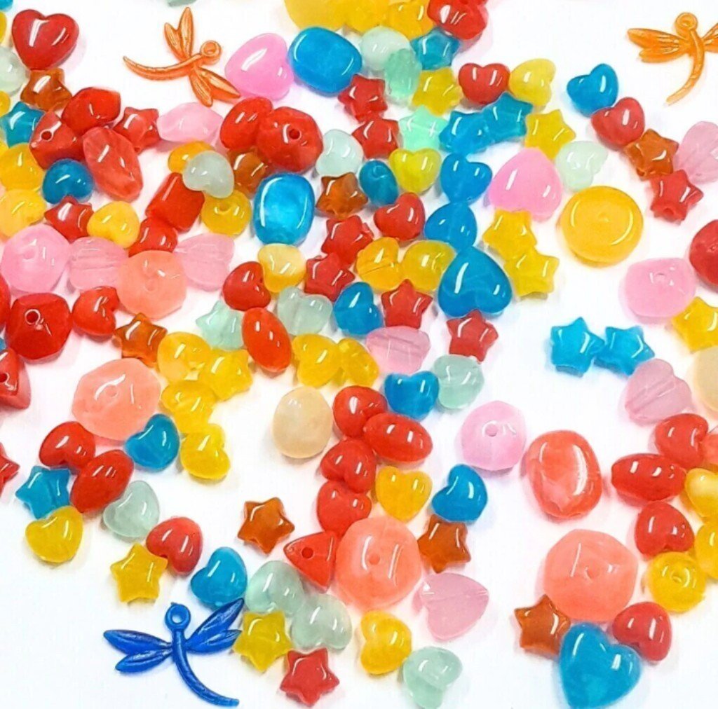 Mix de miçangas plásticas de cores variadas e formatos diversos, como corações, estrelas e libélulas.
