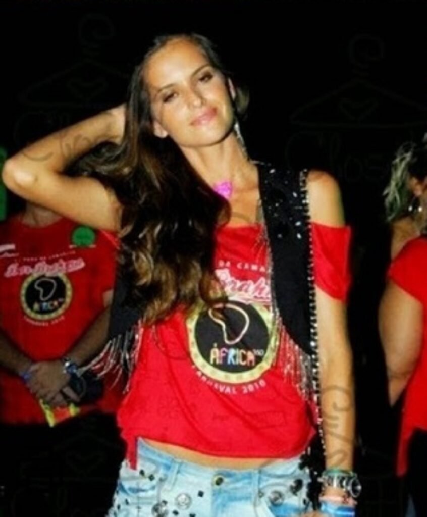Mulher em festa de carnaval com uma camiseta vermelha e colete de franjas, e shorts jeans customizados.