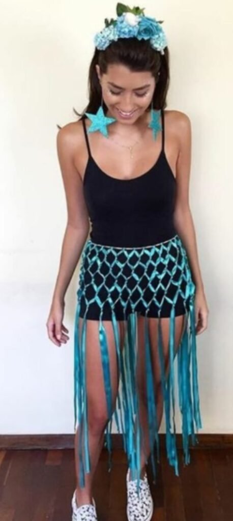 Mulher fantasiada de sereia para o carnaval, com um top preto, saia de franjas azuis, tiara de flores e brincos de estrela.