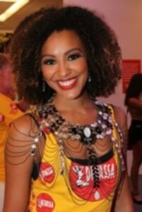 Mulher, usando uma fantasia de carnaval com abadá amarelo e uma joia prateada.