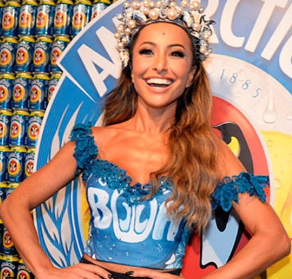 Mulher com uma fantasia de carnaval inspirada em uma lata de refrigerante, com um cocar de pérolas na cabeça.