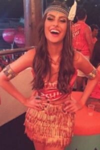 Mulher com uma fantasia de carnaval de índia, com um top de abadá, saia de franjas, e acessórios na cabeça e nos braços.