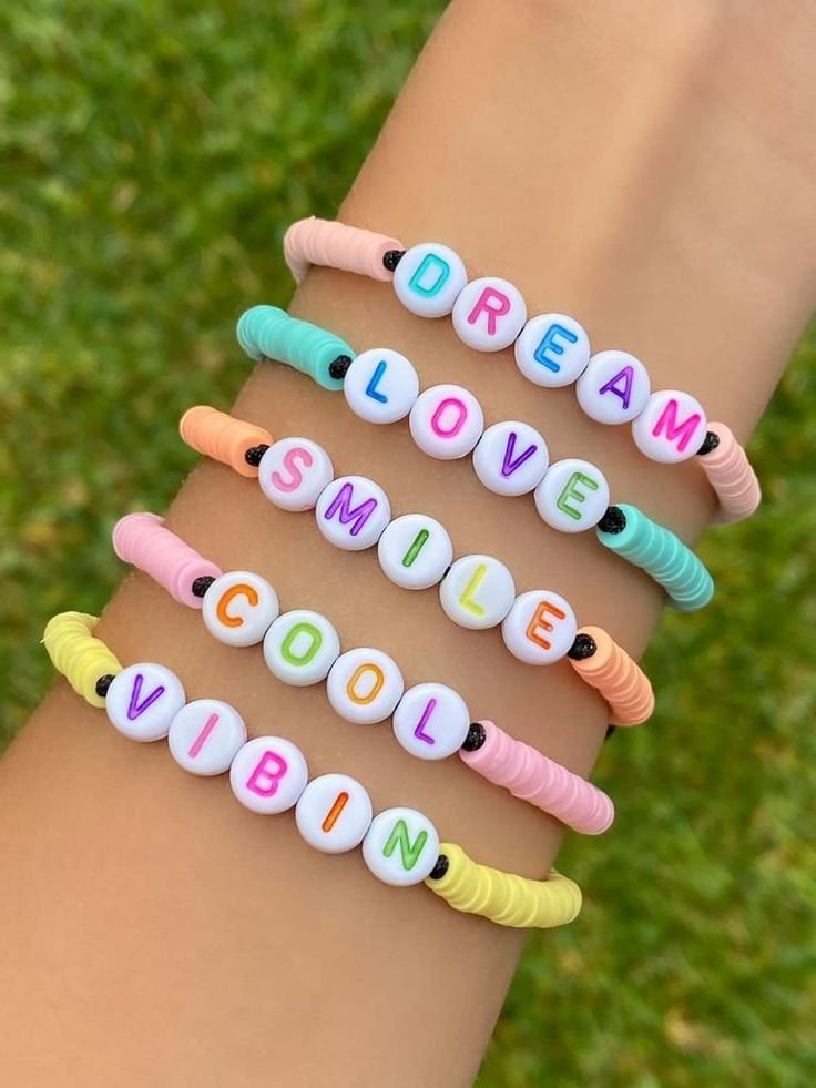 Cinco pulseiras coloridas com miçangas redondas e letras formando as palavras DREAM, LOVE, SMILE, COOL, e VIBIN.