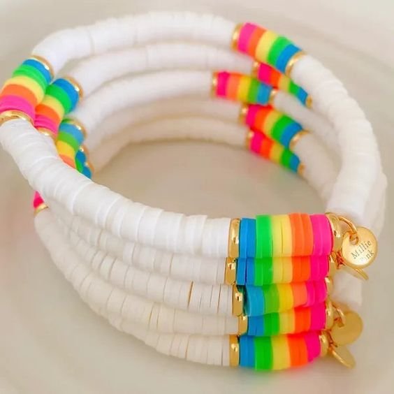 Coleção de pulseiras brancas com faixas coloridas e pingentes dourados.