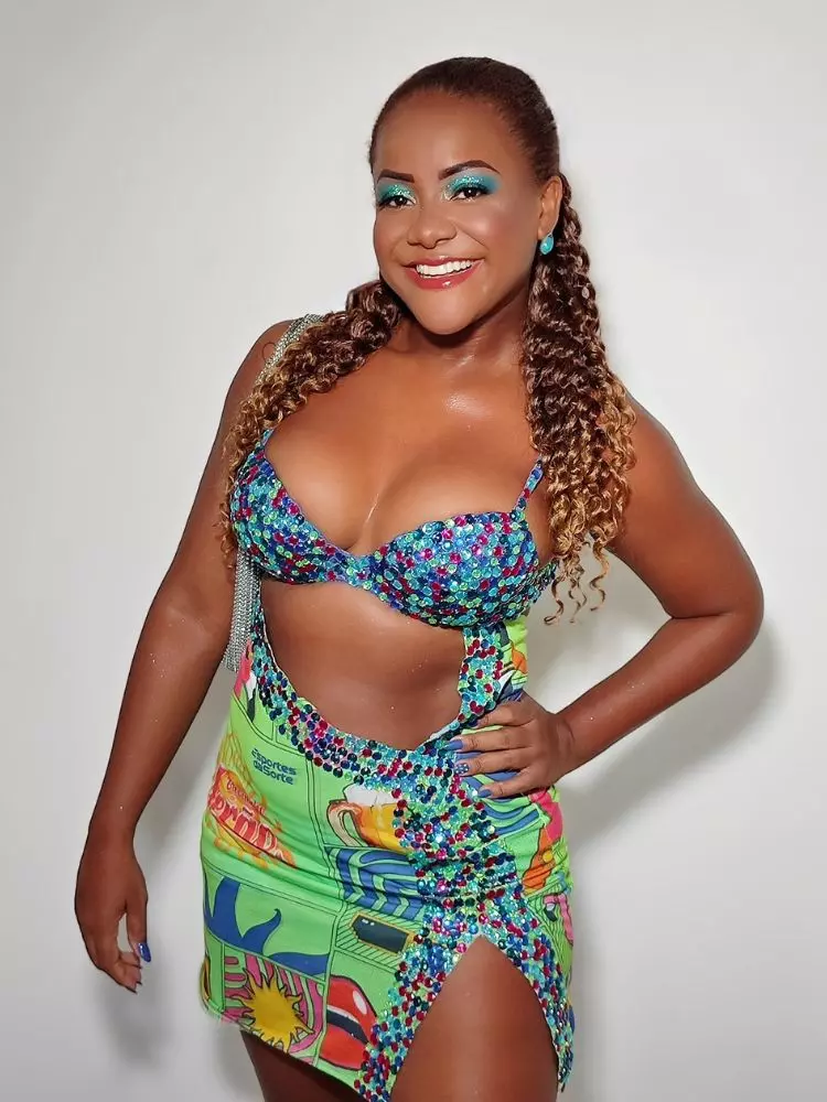 Mulher sorridente com uma fantasia de carnaval colorida, de um abadá customizado com brilho e decote na cintura.