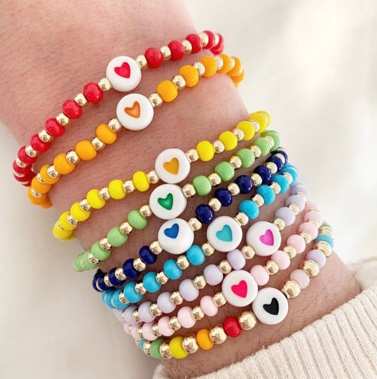 Pulso com uma coleção de pulseiras de miçangas coloridas com pingentes de coração branco.