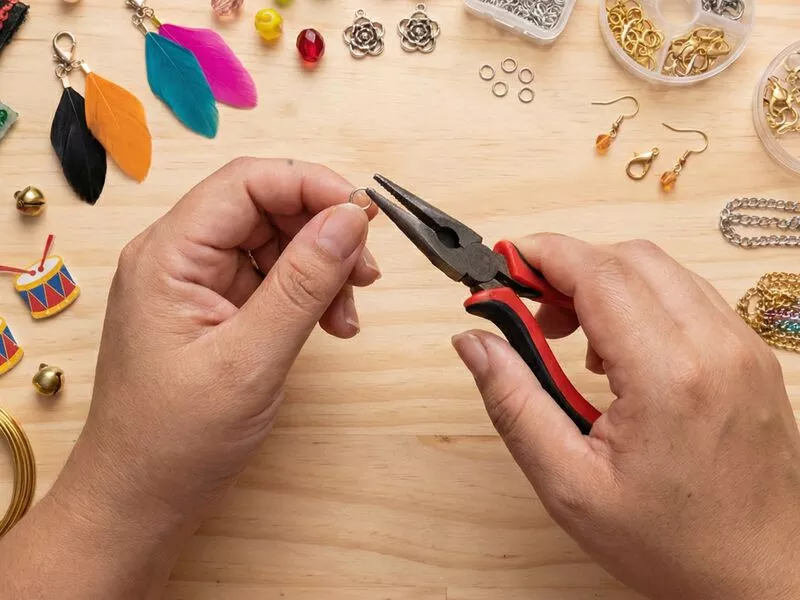 Mão segurando alicate em mesa de bijuterias