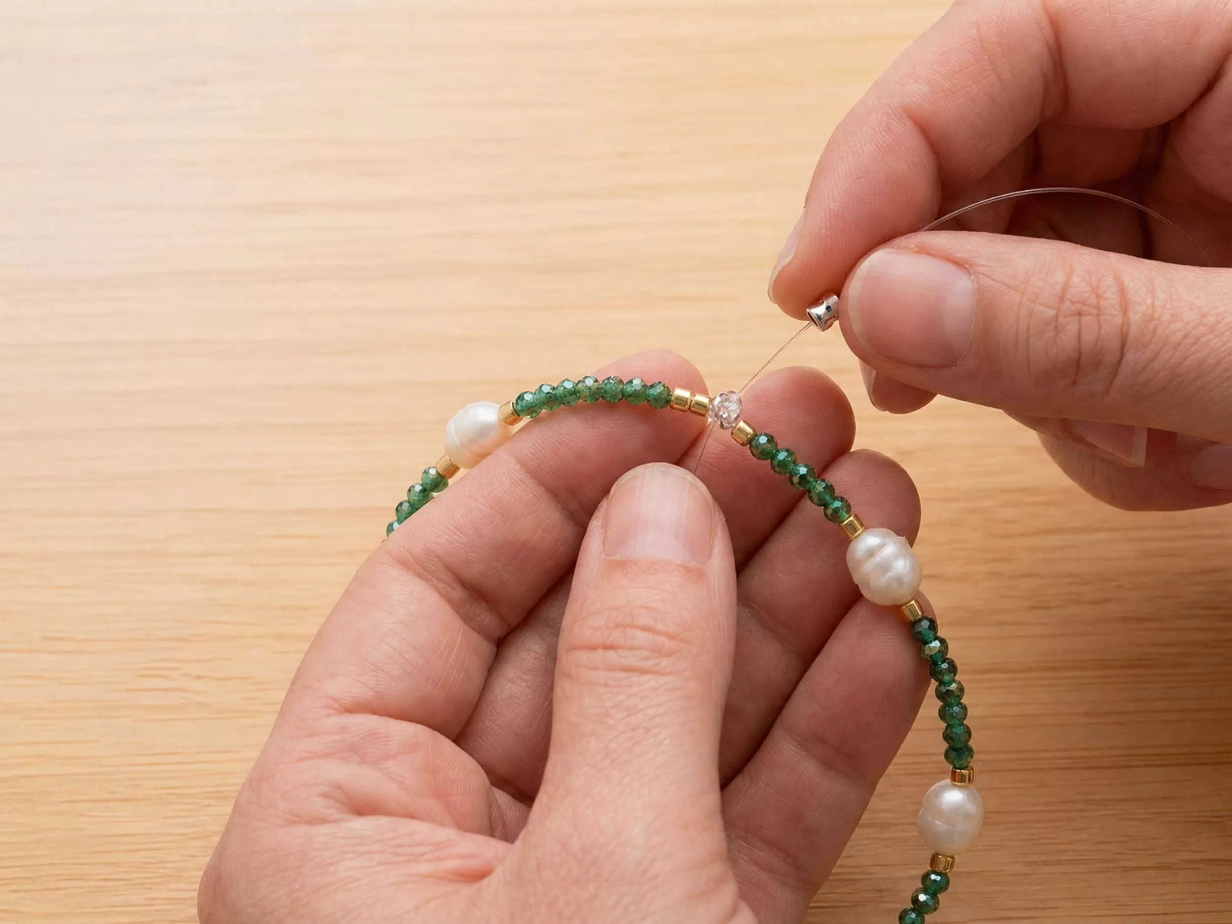 artesão montando colar de pérolas e pedras verdes